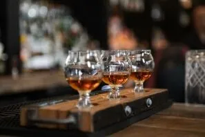 Three whiskey snifter glasses on a wooden flight board at a bar, amber liquid catching the light.