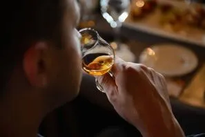 Close-up of a person holding a glass of amber whiskey near their lips in a dimly lit setting.