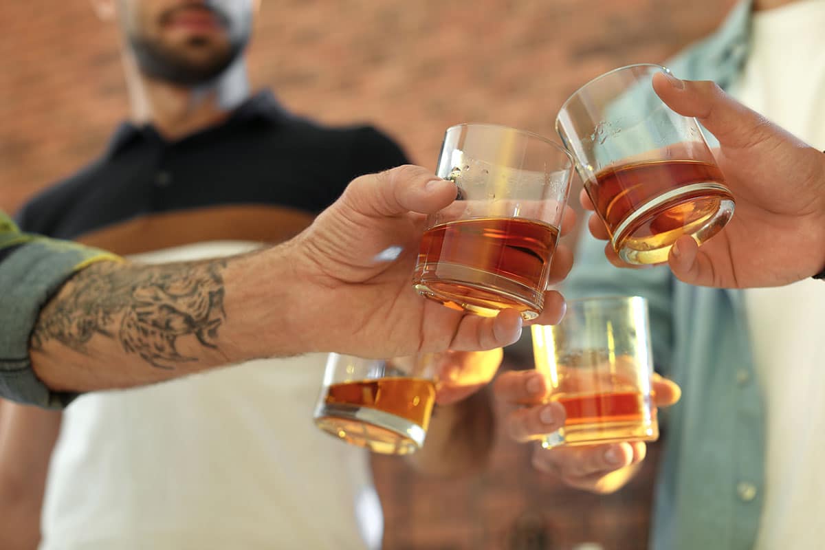A group of friends toasting with glasses of whiskey outdoors, raising their drinks together.